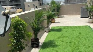 Une terrasse sur le toit, agrémentée de gazon synthétique, de plantes en pot et d’une antenne parabolique.