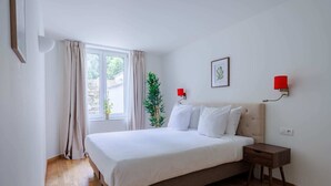 Een slaapkamer met een groot bed, twee nachtkastjes, een raam met gordijnen, een kamerplant en twee wandlampen.