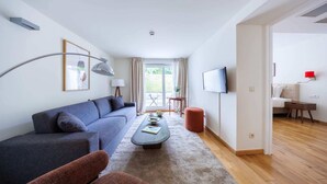 Een moderne woonkamer met een grijze bank, een salontafel en een televisie. Er staat een rode poef en ligt een houten vloer.