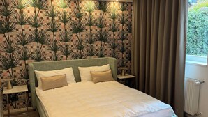 A bedroom with a bed, nightstands, a window with curtains, and a patterned wallpaper.