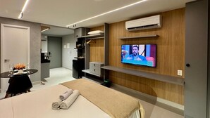 A modern hotel room with a bed, a TV mounted on the wall, a small desk with a chair, and a wooden panel wall. - Vert House (Joao Pessoa)