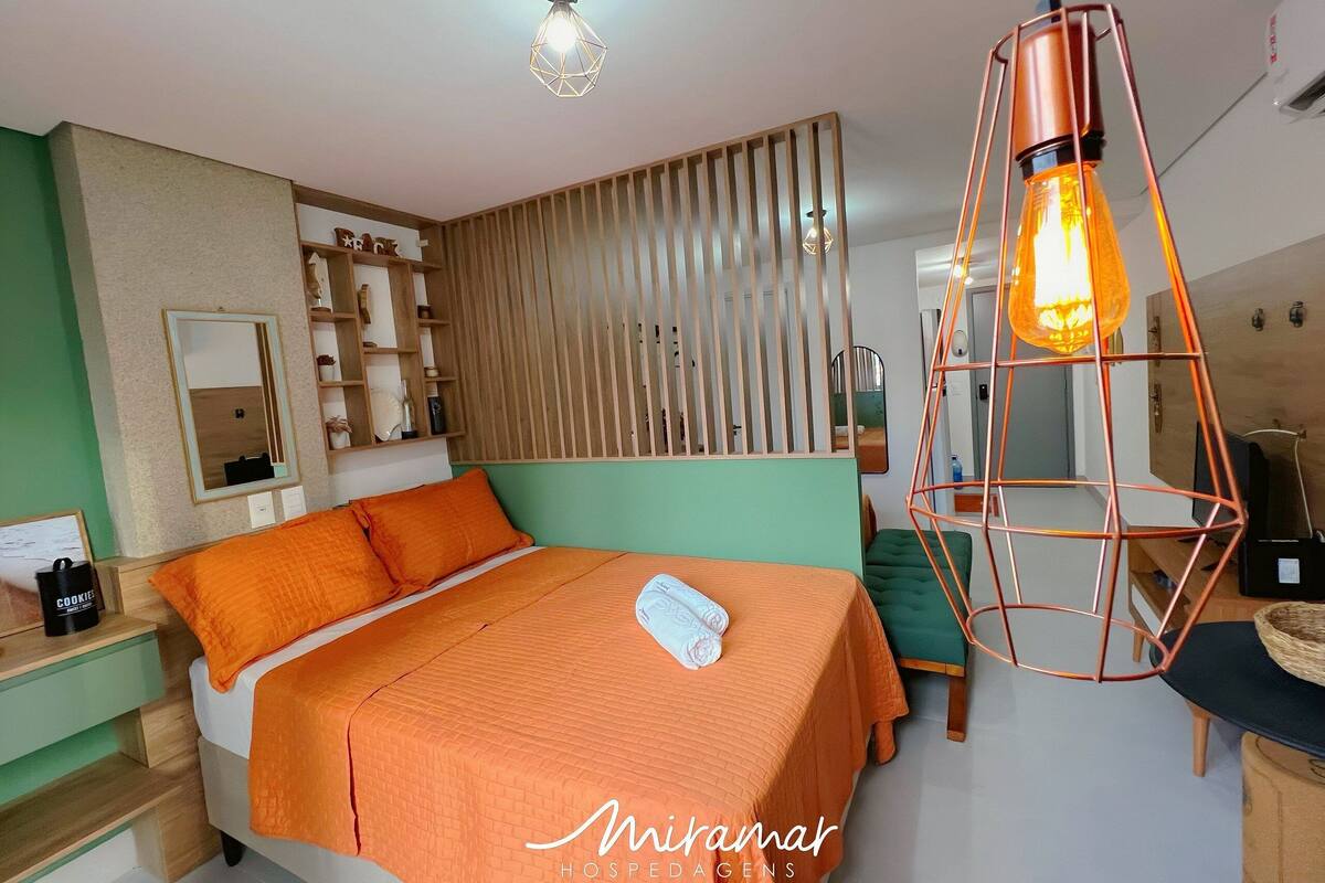 A hotel room with a bed, a nightstand, a mirror, and a hanging light fixture.