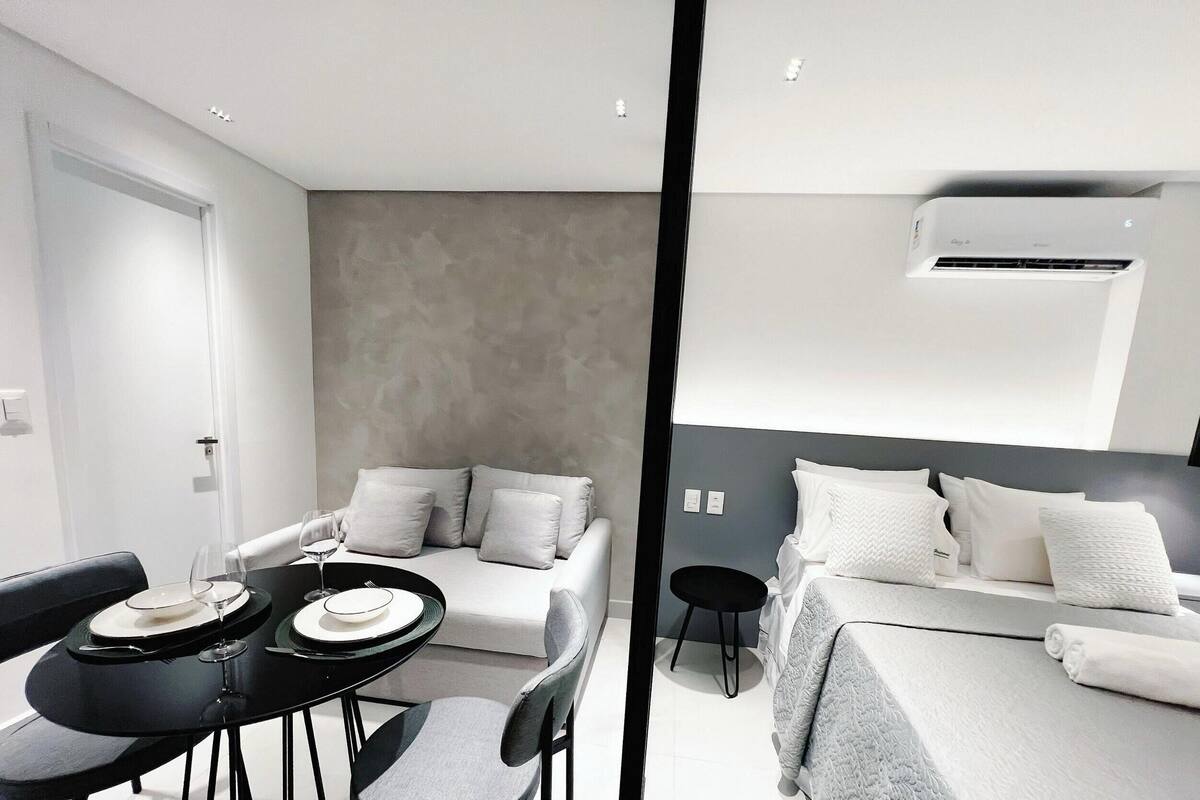 A modern hotel room with a dining area, a sofa, a bed, and an air conditioning unit.