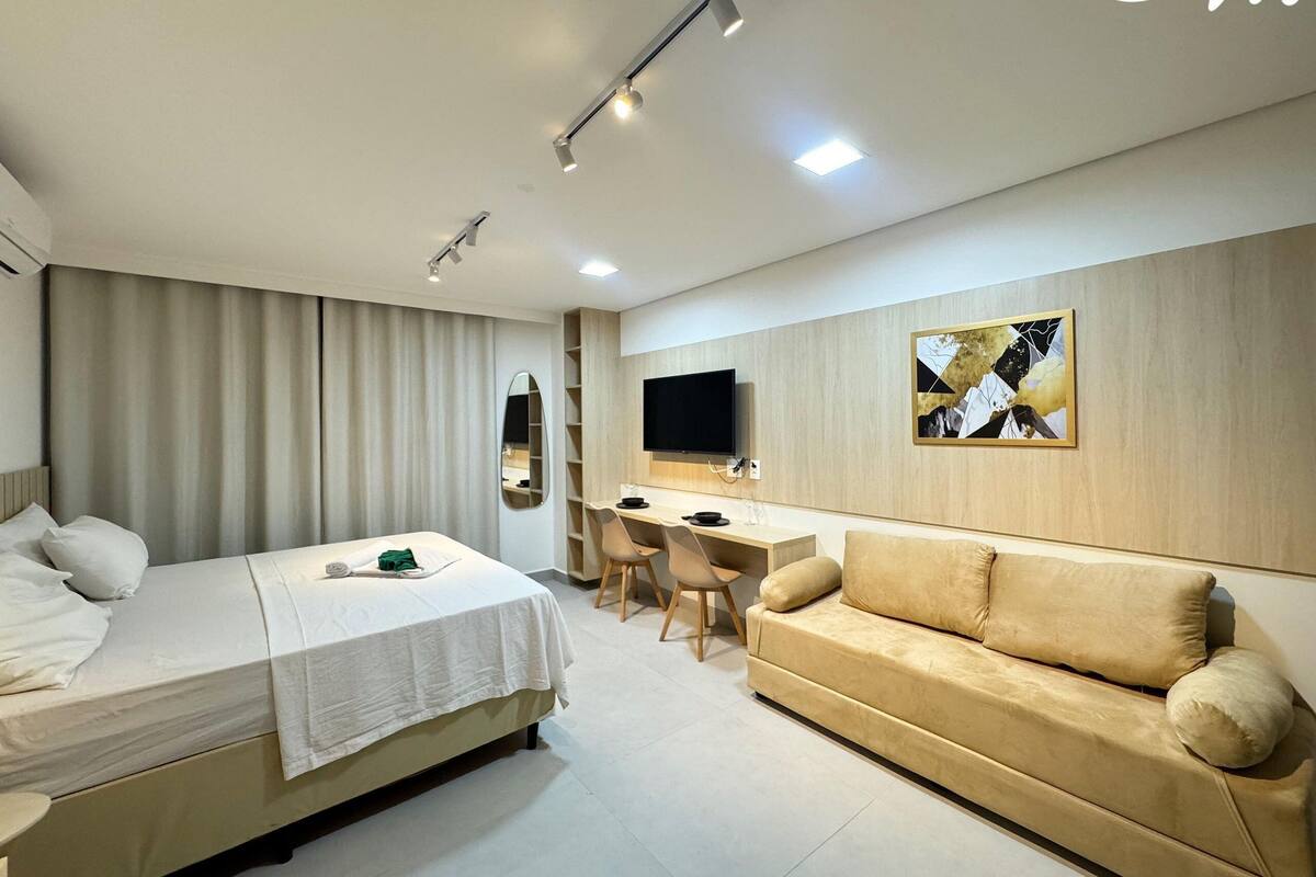 A modern hotel room with a bed, a sofa, a desk, and a TV.