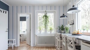 Una cucina con carta da parati a righe, un termosifone bianco, piante pensili e un'area pranzo con sedie e tavolo bianchi.