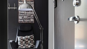 Una sedia moderna con un cuscino a quadretti, una lampada da terra e un muro con un cartello che elenca monumenti di New York.