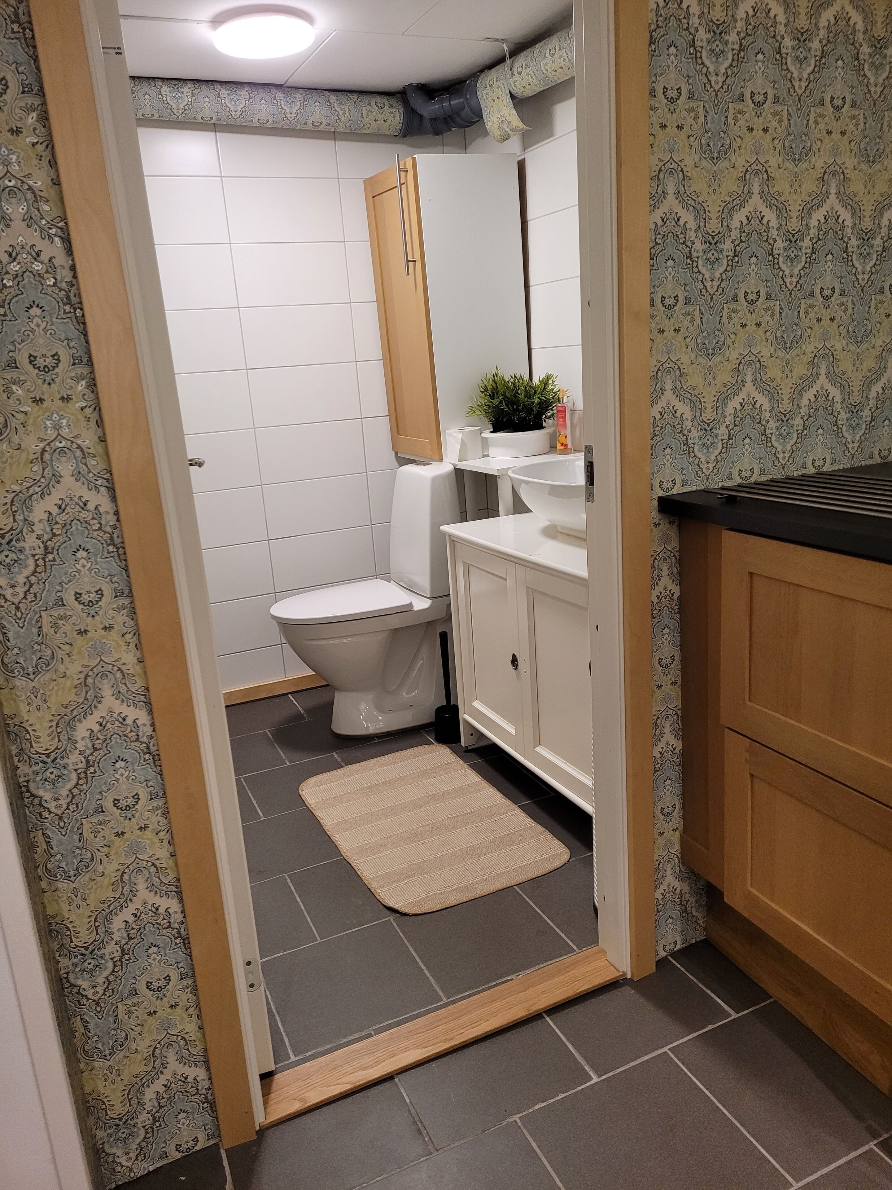 A bathroom with a toilet, sink, mirror, and wooden cabinets.