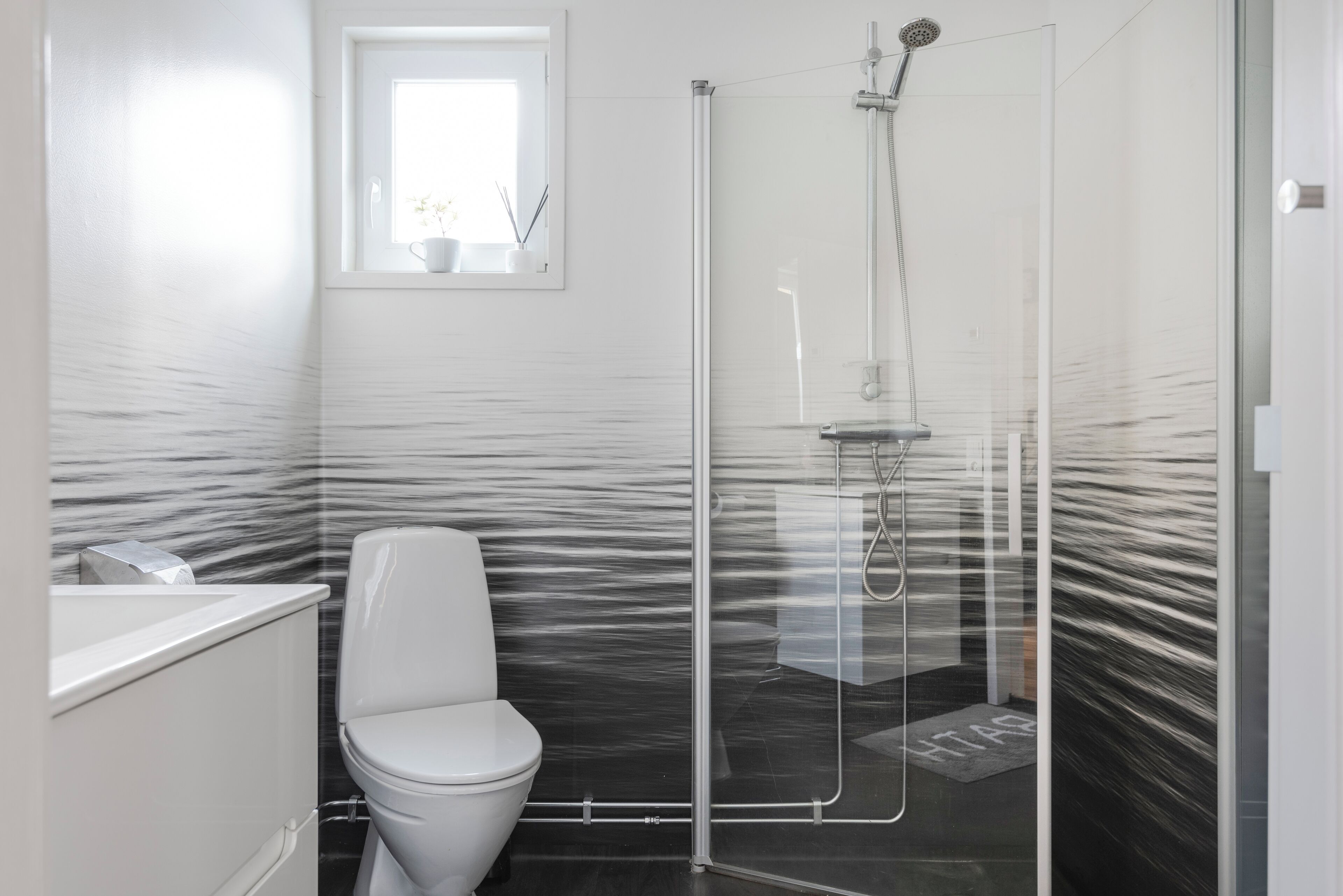 A modern bathroom with a glass shower enclosure, a white toilet, and a marble-patterned wall.
