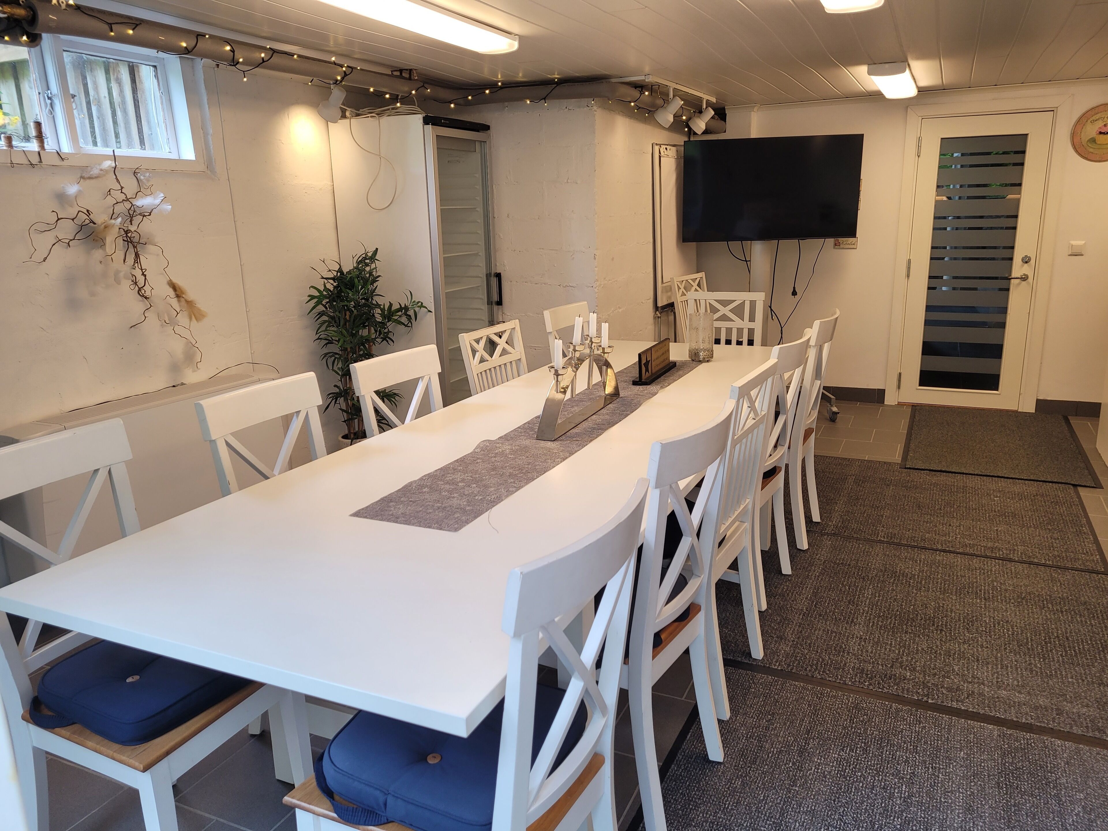 A conference room with a long table, white chairs, a flat-screen TV, and a potted plant.