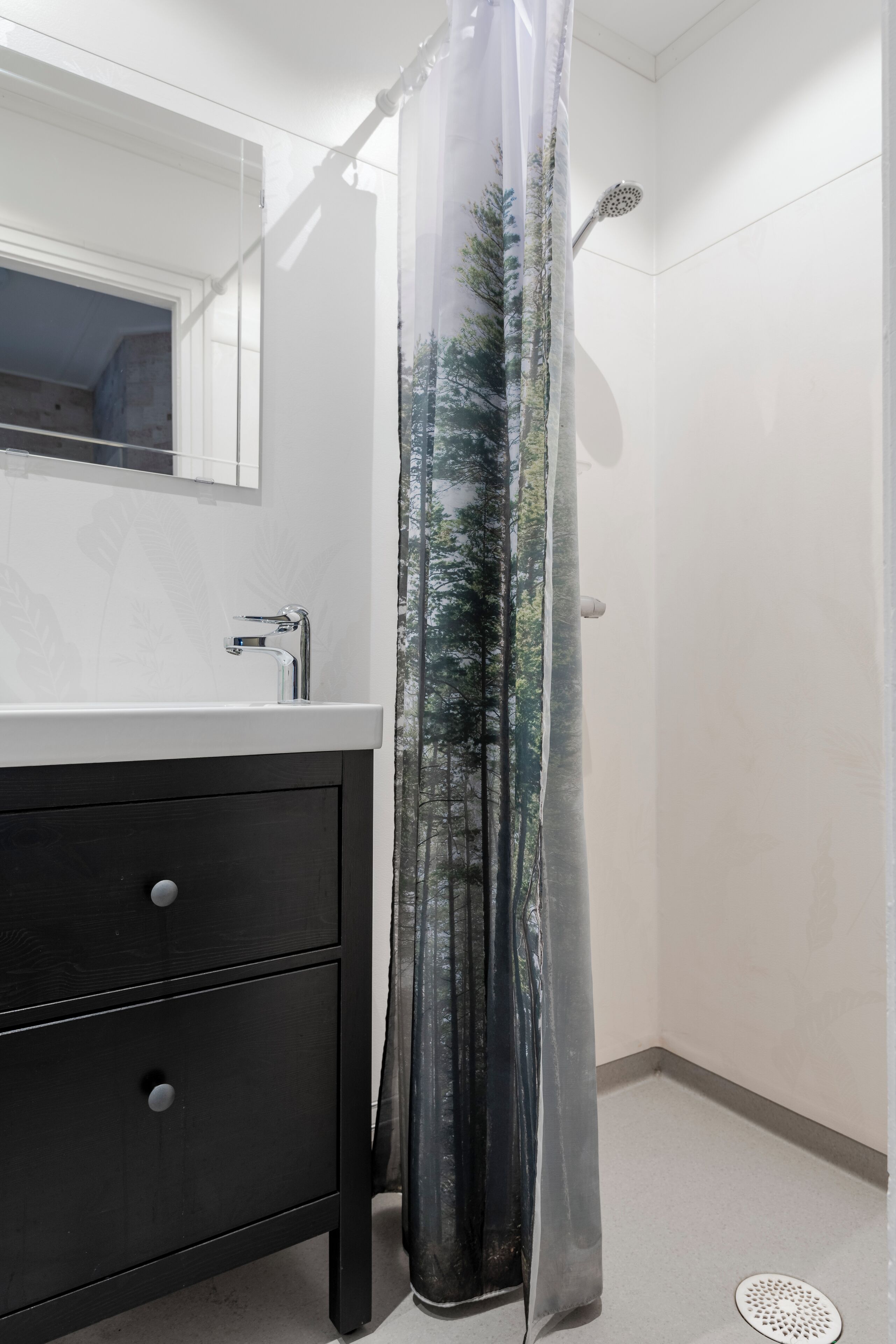 Ein Badezimmer mit weißem Waschbecken, dunklem Holzschrank und einer Duschvorhang mit Waldmusterung.