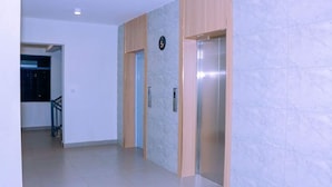 Een hal met een marmeren muur, een houten paneel en een moderne lift.