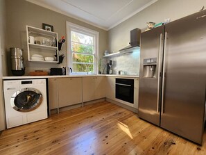 A compact kitchen with a washing machine, a refrigerator, and a window providing natural light.