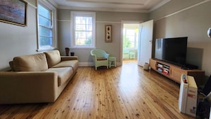 Een woonkamer met een bank, een televisie en een houten vloer.