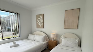Camera d'albergo con due letti, una finestra con tende, una lampada da comodino e opere d'arte alle pareti.