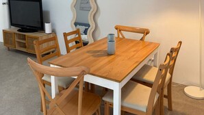 Zona pranzo con tavolo e sedie in legno, televisione su un mobile, una lampada e uno specchio a parete.