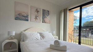 Una camera d'albergo con un letto grande, biancheria da letto bianca, un comodino con una lampada e un'opera d'arte appesa al muro.