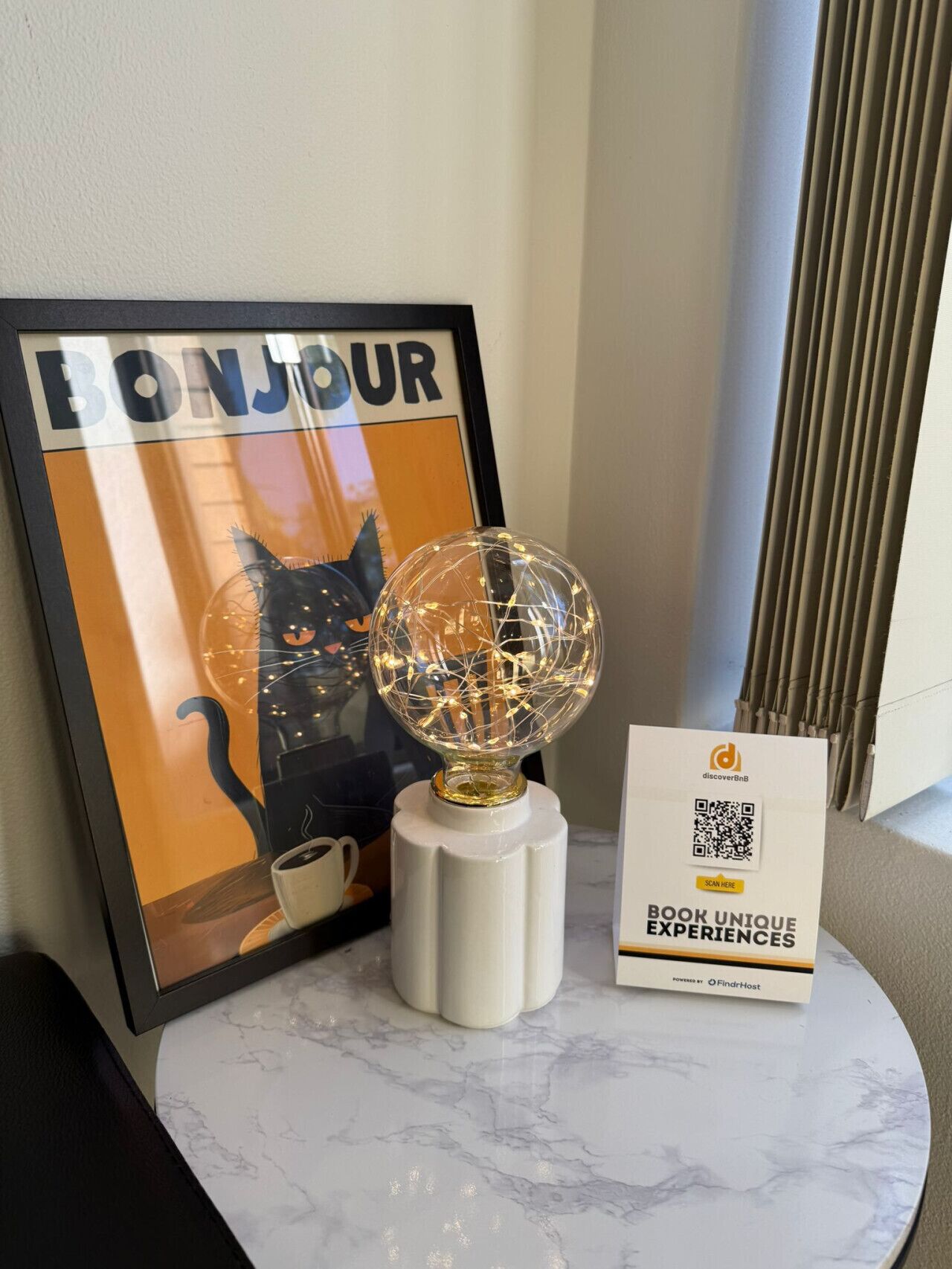 A framed 'BONJOUR' poster with a cat silhouette, a decorative globe, and a QR code sign on a marble table.