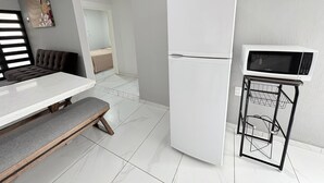 A modern kitchen with a white refrigerator, a microwave on a cart, and a bench. - Residencial Gran Cobae Triplex A (Tonalá)