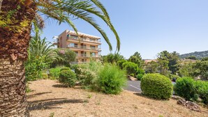 A multi-story building with balconies, surrounded by palm trees and various shrubs. - Le Bosquet - Appt Climatisé, Proche Plage (Sainte-Maxime)