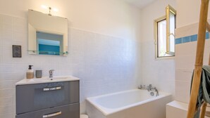 A bathroom with a bathtub, a toilet, a vanity with drawers, a mirror, and a window. - Le Bosquet - Appt Climatisé, Proche Plage (Sainte-Maxime)