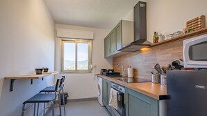 A modern kitchen with a built-in oven, a microwave, and a sink. There is a window providing natural light and a view of the outdoors. - Le Bosquet - Appt Climatisé, Proche Plage (Sainte-Maxime)