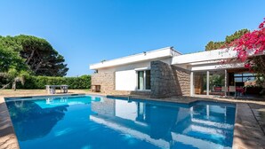 Un área de piscina moderna con un edificio de piedra, piscina azul cristalina y exuberante follaje.