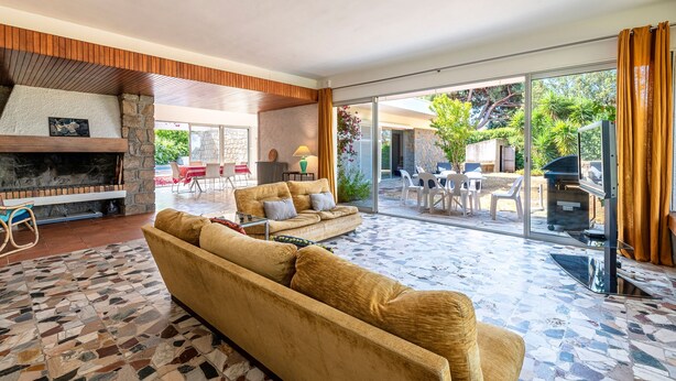 Una sala de estar moderna con chimenea de piedra, un sofá grande y un área de patio con mobiliario exterior.