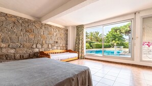 Un dormitorio con pared de piedra, cama, vista a una piscina y puerta corredera de vidrio.