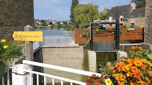 Vista de un canal con un muro de piedra, una valla de madera con jardineras y un letrero que dice "Promenade de la Guette".