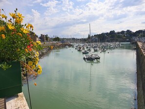 A marina with numerous boats docked, a stone wall, and a flower bed with yellow flowers. - Ô p'tit moulin- Studio vue sur le port (Pléneuf-Val-André)