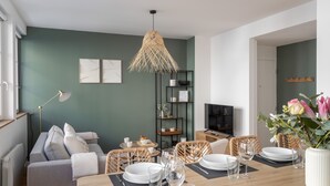 Una sala de estar moderna con comedor, que incluye un sofá, una mesa de comedor con platos y vasos, un televisor y una estantería.