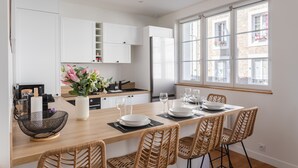 Una cocina moderna con armarios blancos, encimera de madera y un comedor con sillas de mimbre.