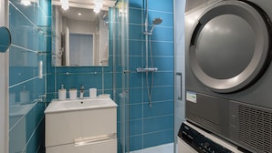 A modern bathroom with a large washing machine, a glass shower enclosure, and a white sink with toiletries. - L'Eperon - Proche Place Charles de Gaulle (Rennes)