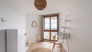 A modern bedroom with a large window, a white dresser, a chair, and a hanging light fixture. - L'Eperon - Proche Place Charles de Gaulle (Rennes)