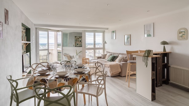 A spacious living area with a dining table set for four, a sofa, and a view of the city. - L'Eperon - Proche Place Charles de Gaulle (Rennes)