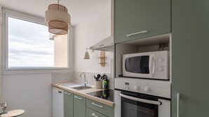 A compact kitchen with a microwave, oven, and dishwasher. It features a window with a view, a sink, and green cabinets. - L'Eperon - Proche Place Charles de Gaulle (Rennes)