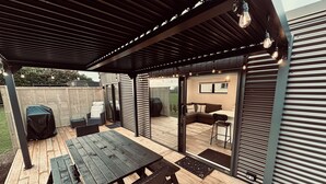 Un patio couvert avec une terrasse en bois, des sièges d’extérieur et un espace barbecue.