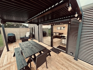 Um alpendre coberto com um deck de madeira, área de estar externa e espaço para churrasco.