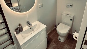 Une salle de bain moderne avec un miroir rond, un lavabo blanc et des toilettes.