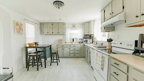 A modern kitchen with light-colored cabinets, a central island with stools, a microwave, and a stove.