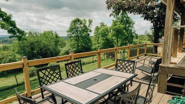 A deck with a table and chairs, overlooking a green landscape.