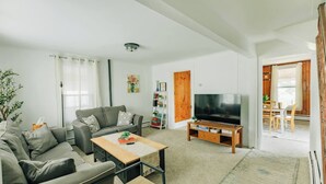 A modern living room with a grey sofa, a wooden coffee table, a flat-screen TV, and a bookshelf.