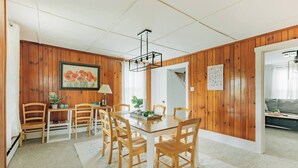 A dining area with a wooden table and chairs, a chandelier, and a framed painting on the wall.