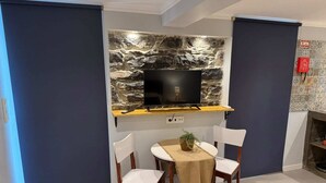 A modern room with a stone wall, a flat-screen TV, a small table with chairs, and a bed with a yellow and grey blanket. -  Refúgio do Nevoeiro (Studio) (Levada Grande)