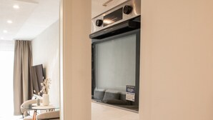 A modern kitchen with a built-in oven and microwave, a small trash bin, and a dining area with a table and chairs. - Central, sunny city apartment near Mercedes - top modern (Sindelfingen)
