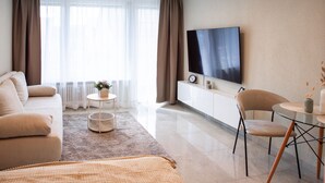 A modern hotel room with a large flat-screen TV, a sofa, a dining table, and a small side table with a plant. - Central, sunny city apartment near Mercedes - top modern (Sindelfingen)