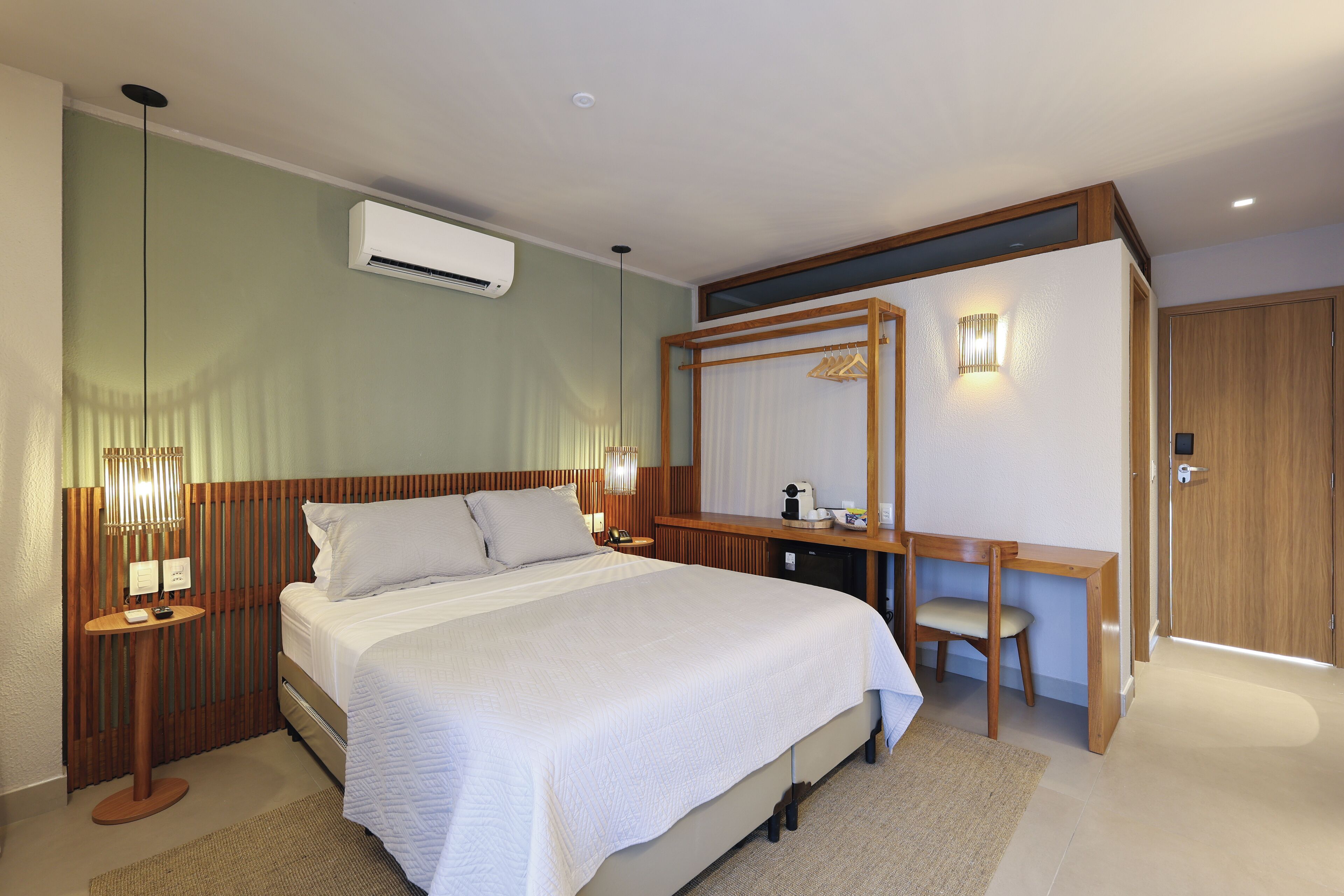 A hotel room with a large bed, a desk, a chair, a wardrobe, and a mirror.