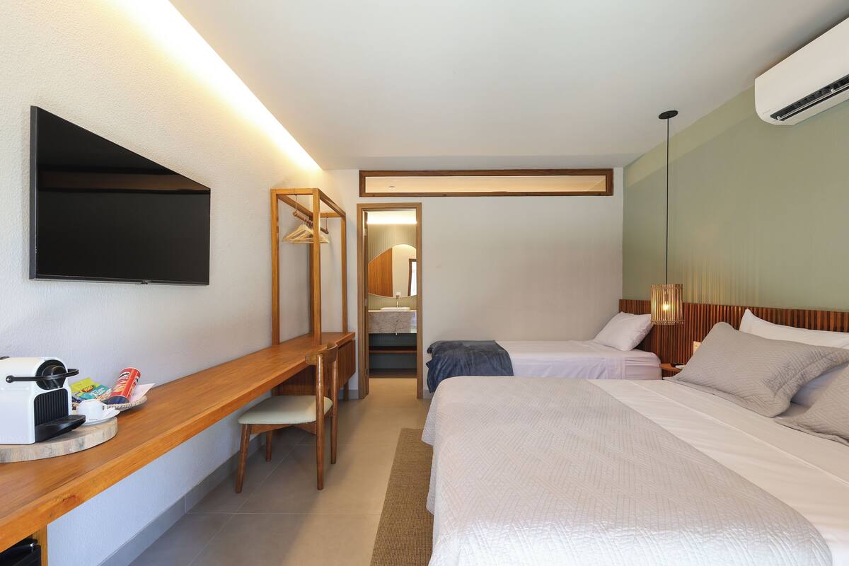 Ein Hotelzimmer mit Bett, Schreibtisch mit Kaffeemaschine, Wand-Fernseher und Spiegel.