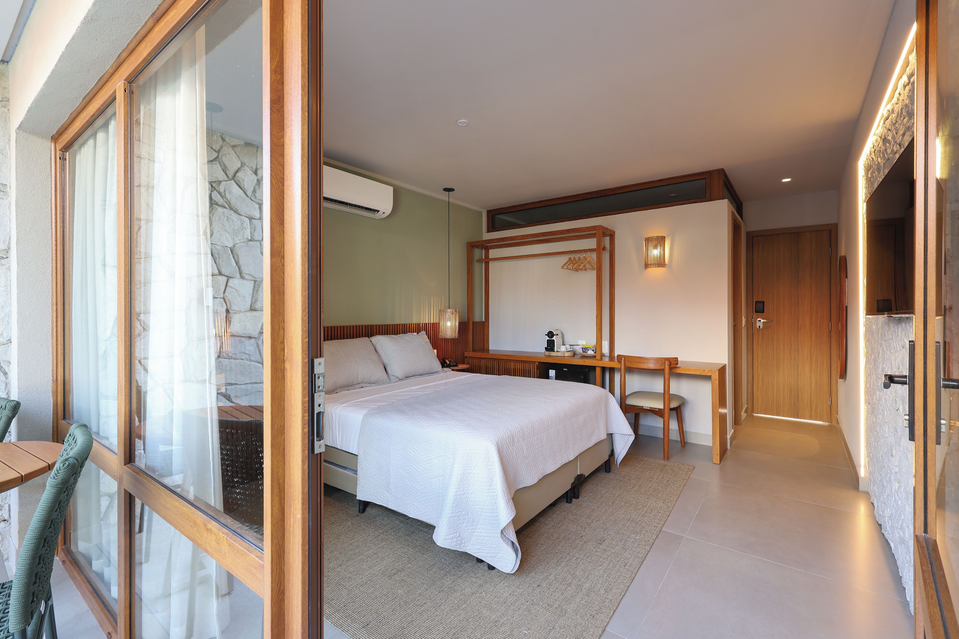 Ein Schlafzimmer mit einem großen Bett, einem Schreibtisch und einem Spiegel. Eine Steinsäule und eine Holztür sind ebenfalls vorhanden.