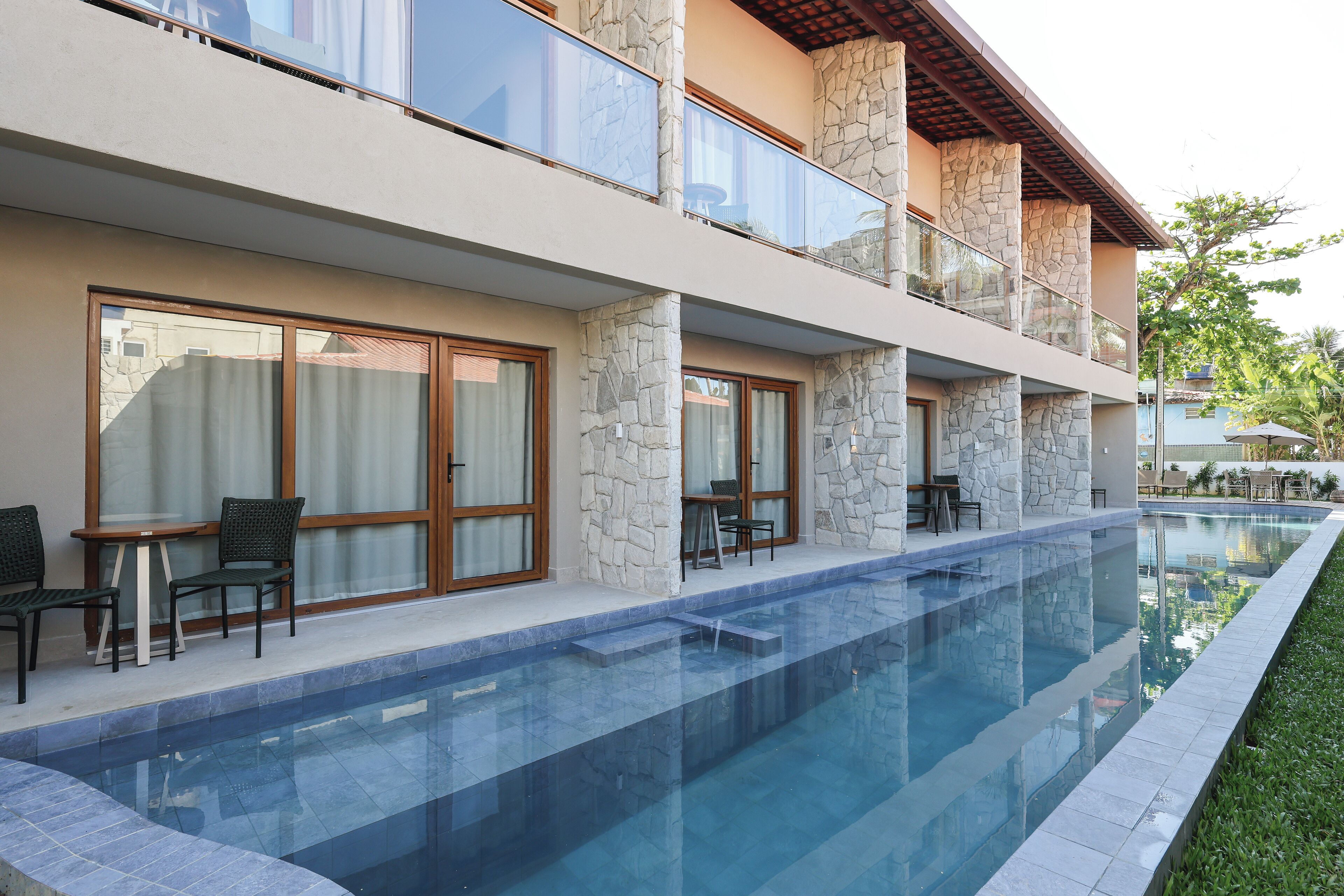 Un hotel moderno con piscina, pilares de piedra y zonas de estar al aire libre.
